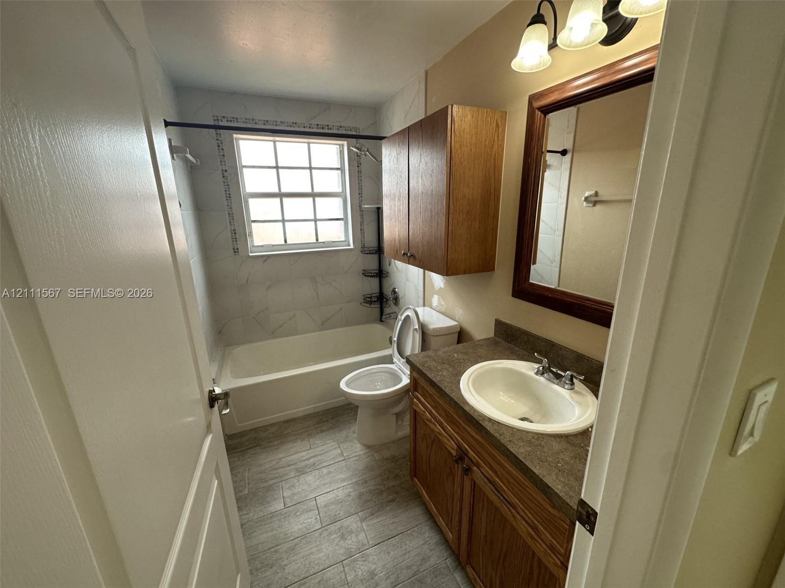 Bathroom featuring a vanity with dark-tone countertop, wood-finish cabinetry, tile-surround tub, and tile flooring