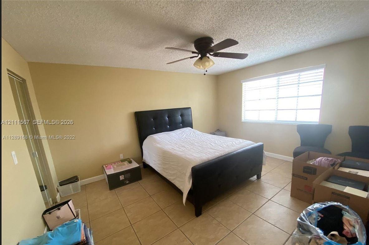 Neutral-toned interior featuring ceramic tile flooring, a central ceiling fan with integrated lighting, and horizontal window blinds