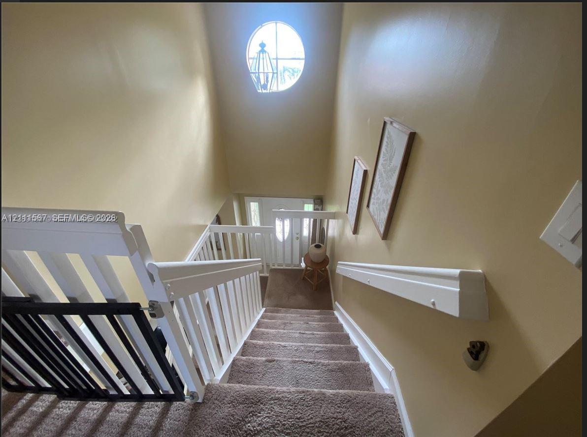 Staircase featuring white balusters, a wooden handrail, carpeted steps, and a circular accent window