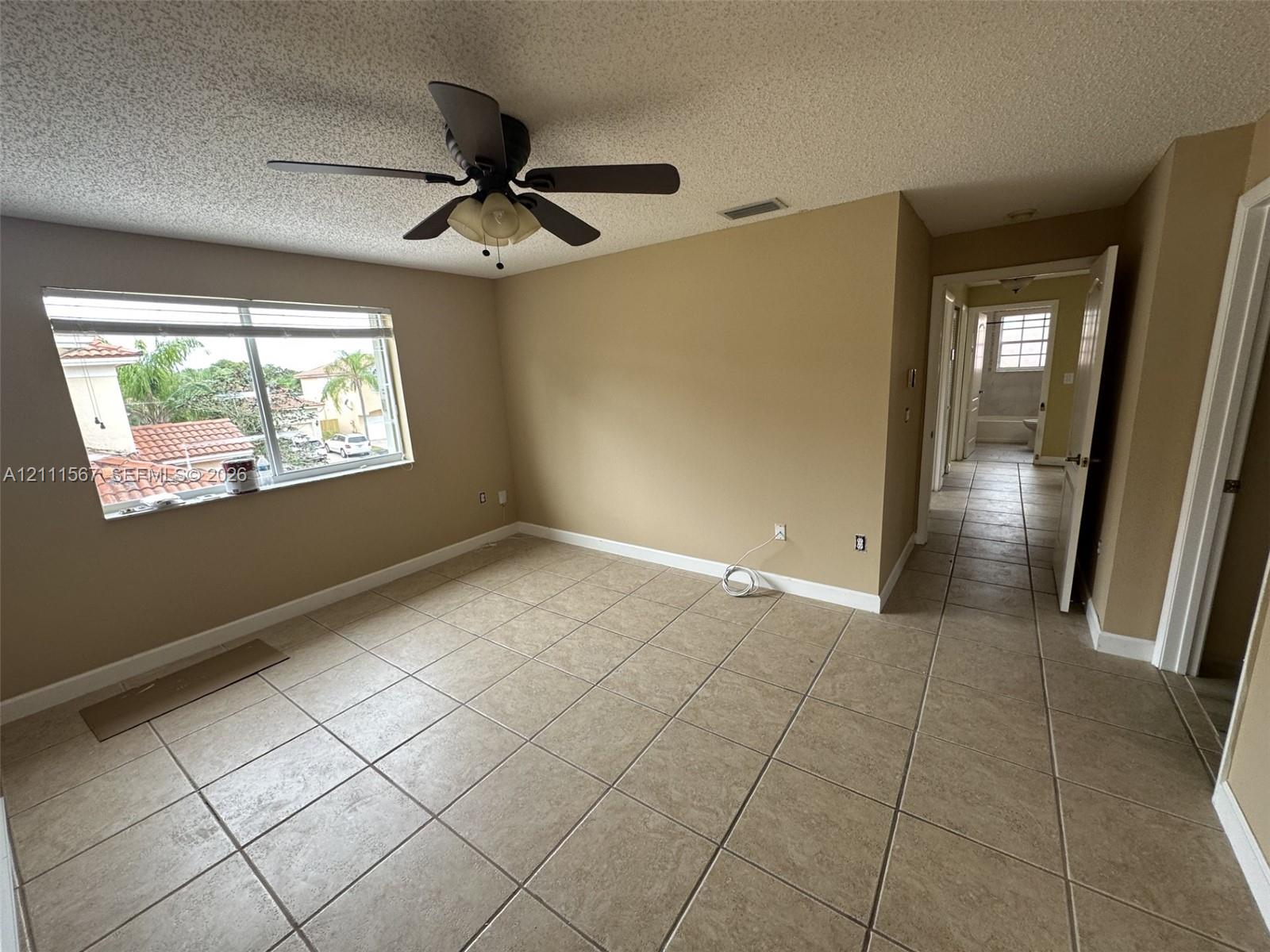 Interior space featuring large-format neutral floor tile, a ceiling fan with integrated lighting, and a window with exterior residential scenery