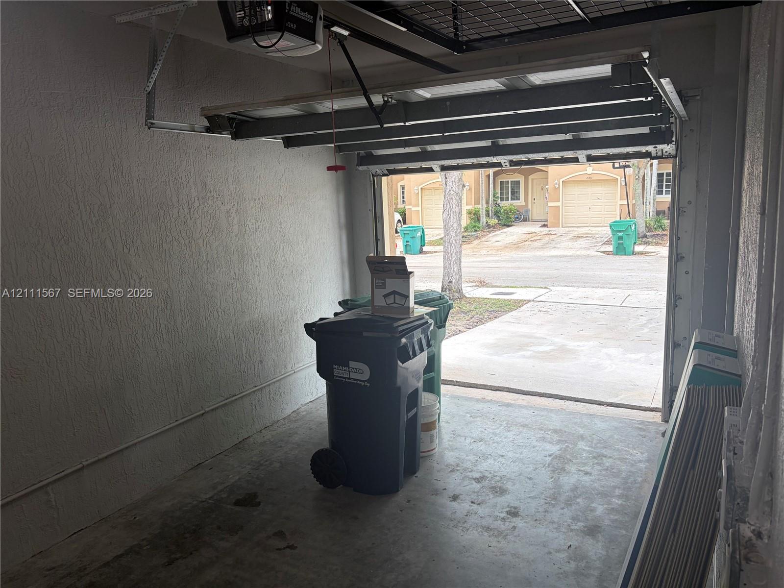 Enclosed garage featuring a concrete floor, textured walls, and an overhead automatic door opener