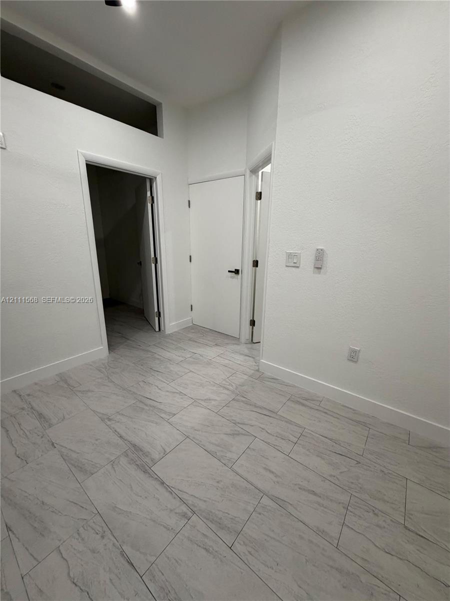 Neutral interior featuring large-format stone-finish floor tiling, high ceilings with a transom window, and solid-core doors with matte black hardware