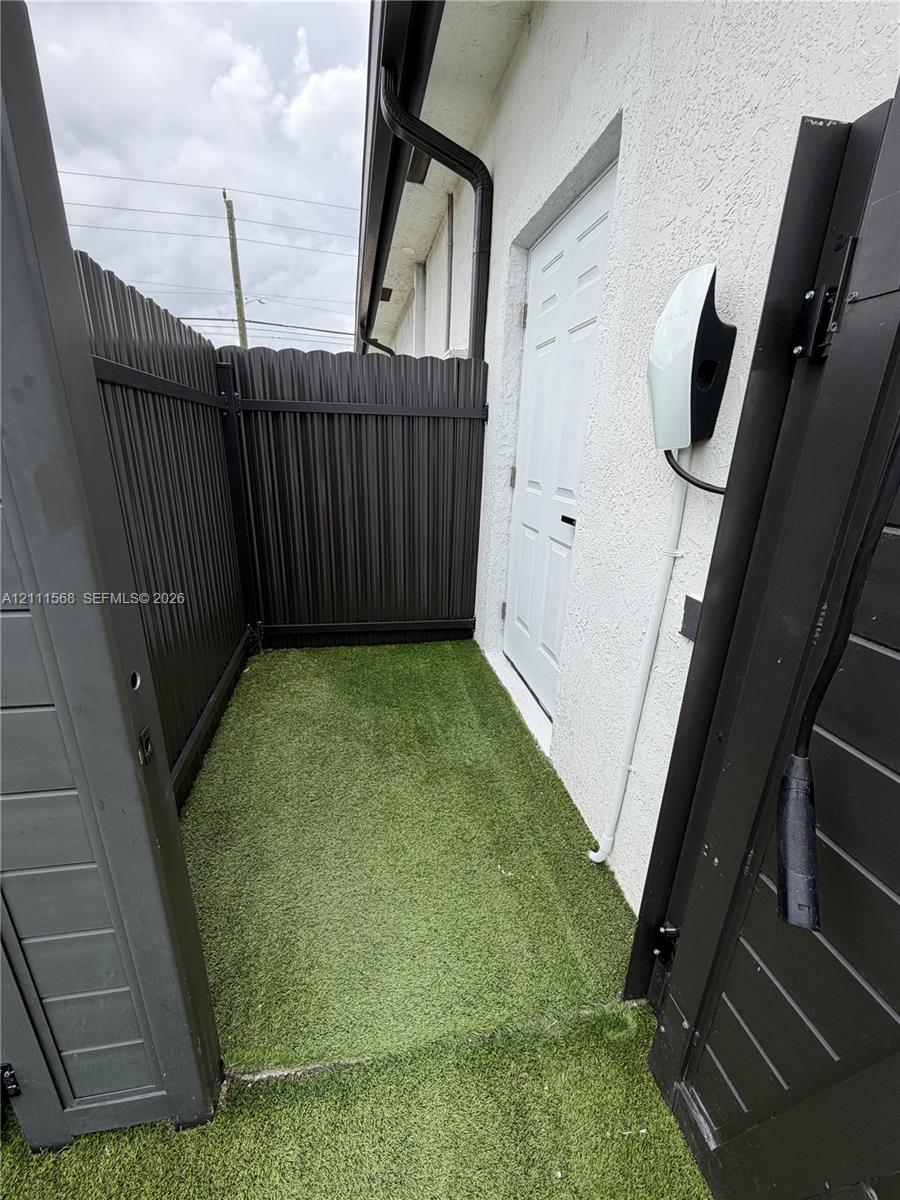 Stucco exterior wall featuring an electric vehicle charging station, synthetic turf surface, and dark-finished privacy fencing Stucco exterior wall featuring an electric vehicle charging station, synthetic turf surface, and dark-finished privacy fencing