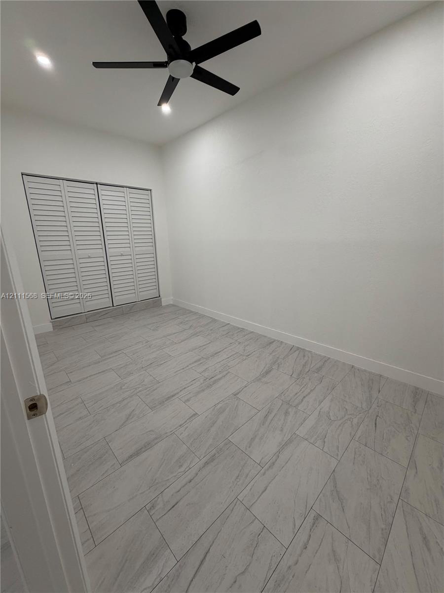 Room featuring tile flooring, louvered-panel closet doors, and a matte black ceiling fan with integrated lighting