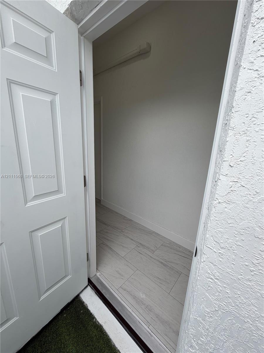Six-panel interior door with light-colored wood-finish flooring and textured stucco exterior wall