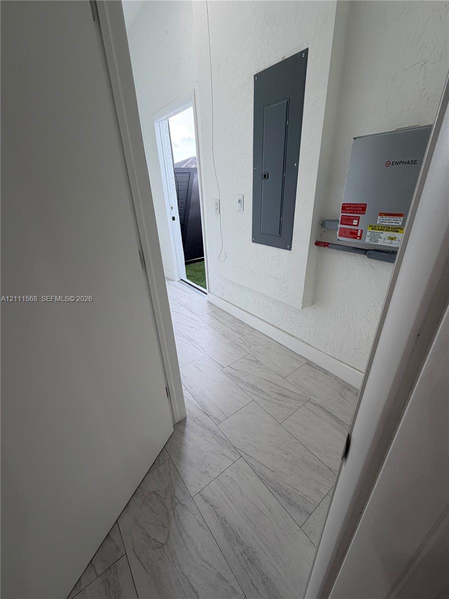 Light-toned ceramic tile flooring, textured wall finishes, and integrated electrical service panel with energy monitoring equipment