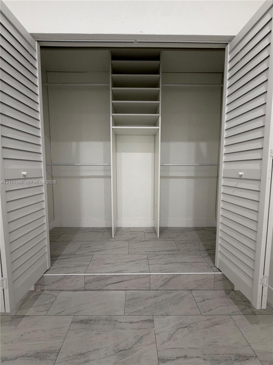 Closet featuring louvered bifold doors, tile flooring, built-in shelving, and dual hanging rods