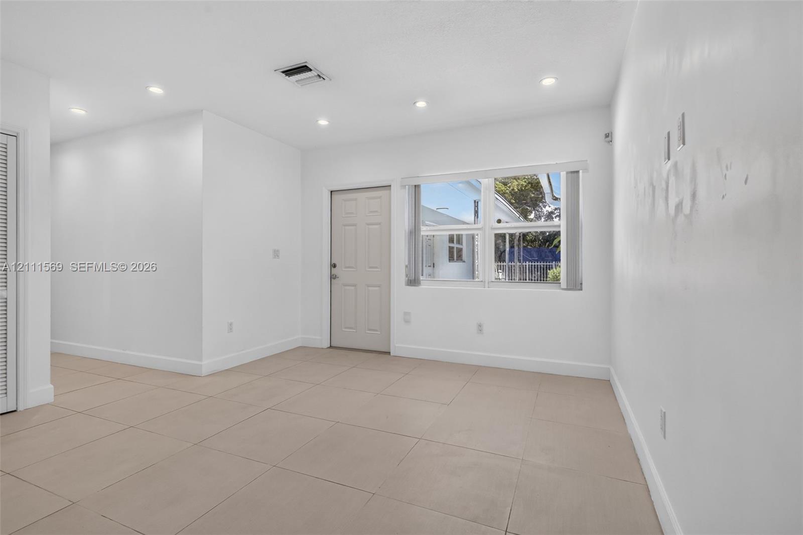 Neutral-toned tile flooring, recessed ceiling lighting, and a multi-pane window with vertical blinds