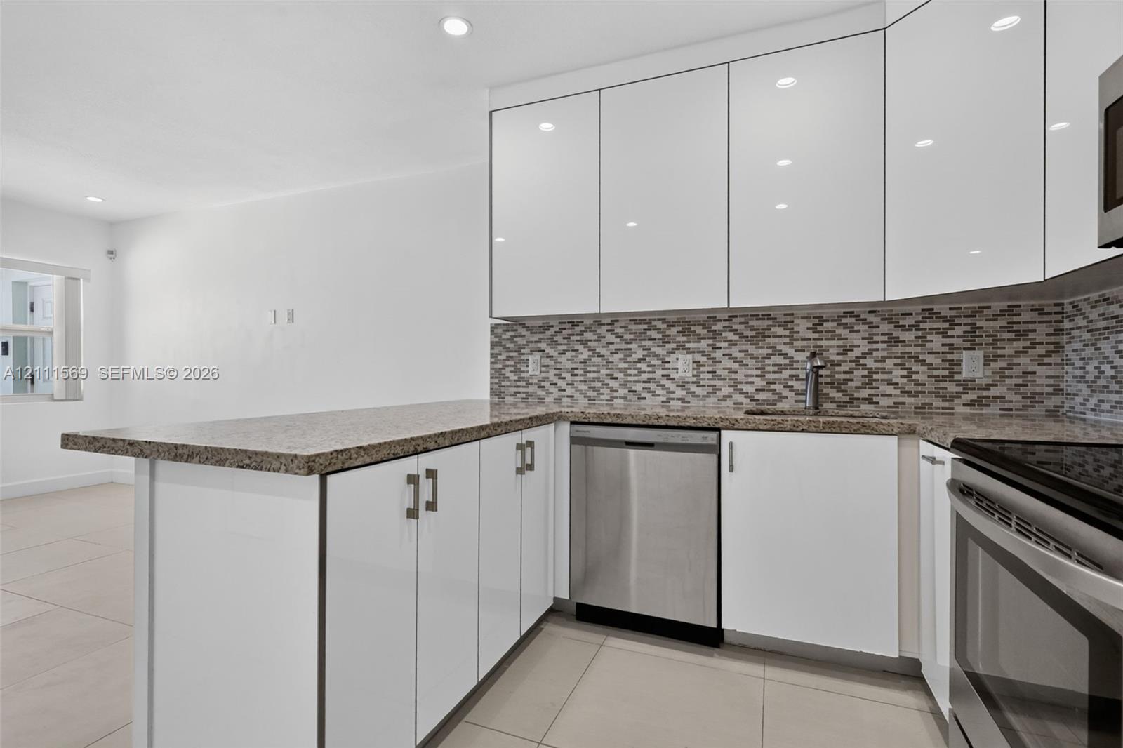 Kitchen featuring white high-gloss cabinetry, stone-finish countertops, stainless steel appliances, mosaic tile backsplash, and recessed lighting