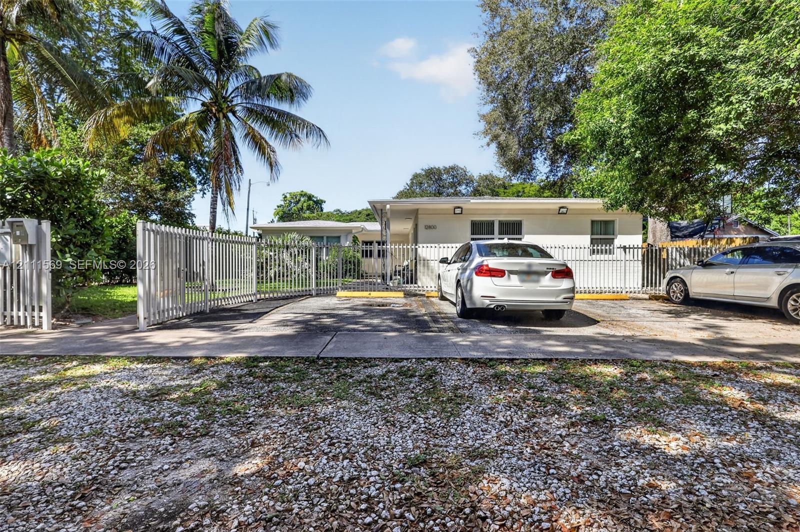 Single-story exterior featuring a concrete facade, paved parking area, metal fencing, and mature landscaping