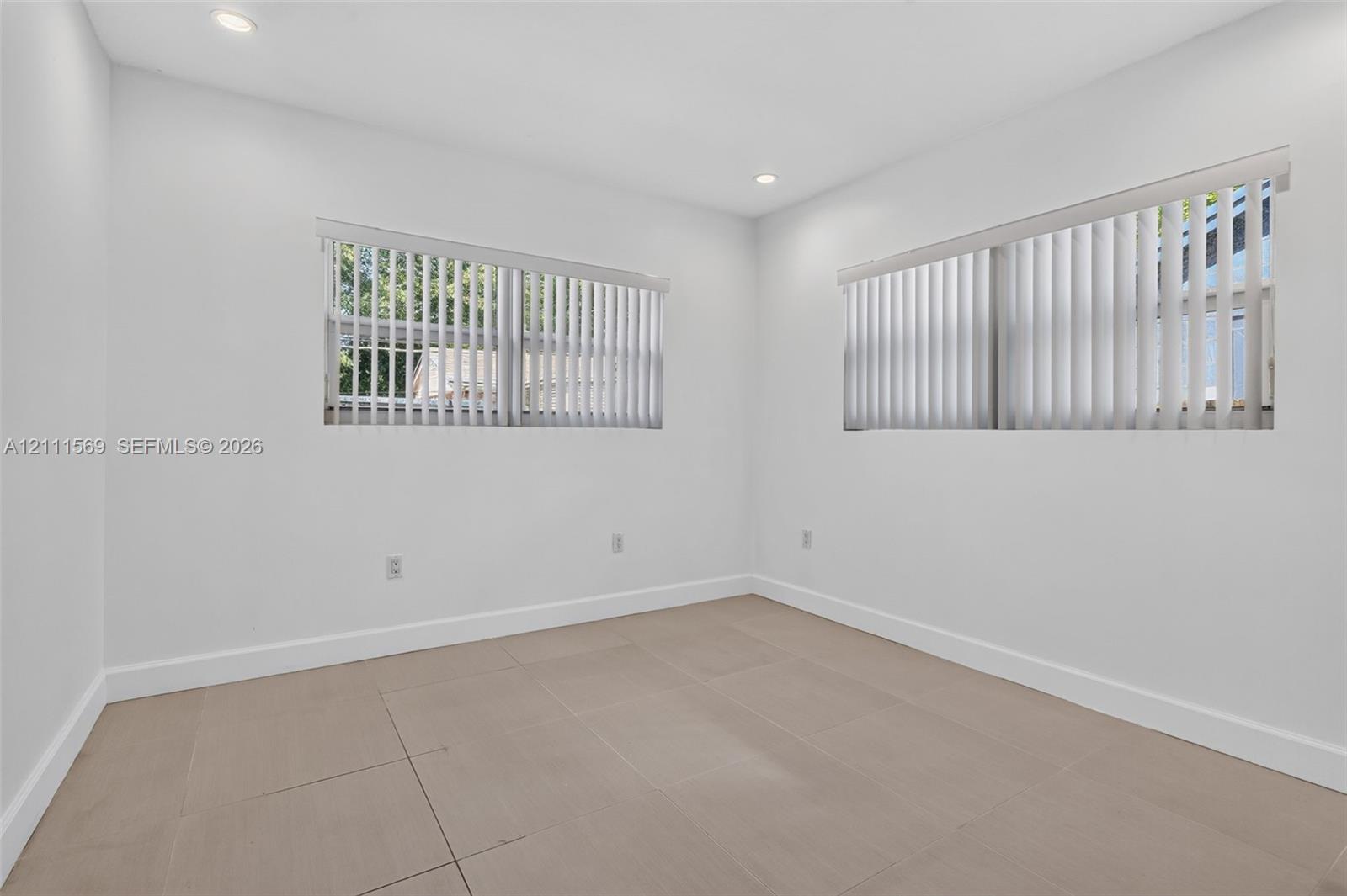 Neutral-toned tile flooring, recessed ceiling lighting, and windows featuring vertical blinds