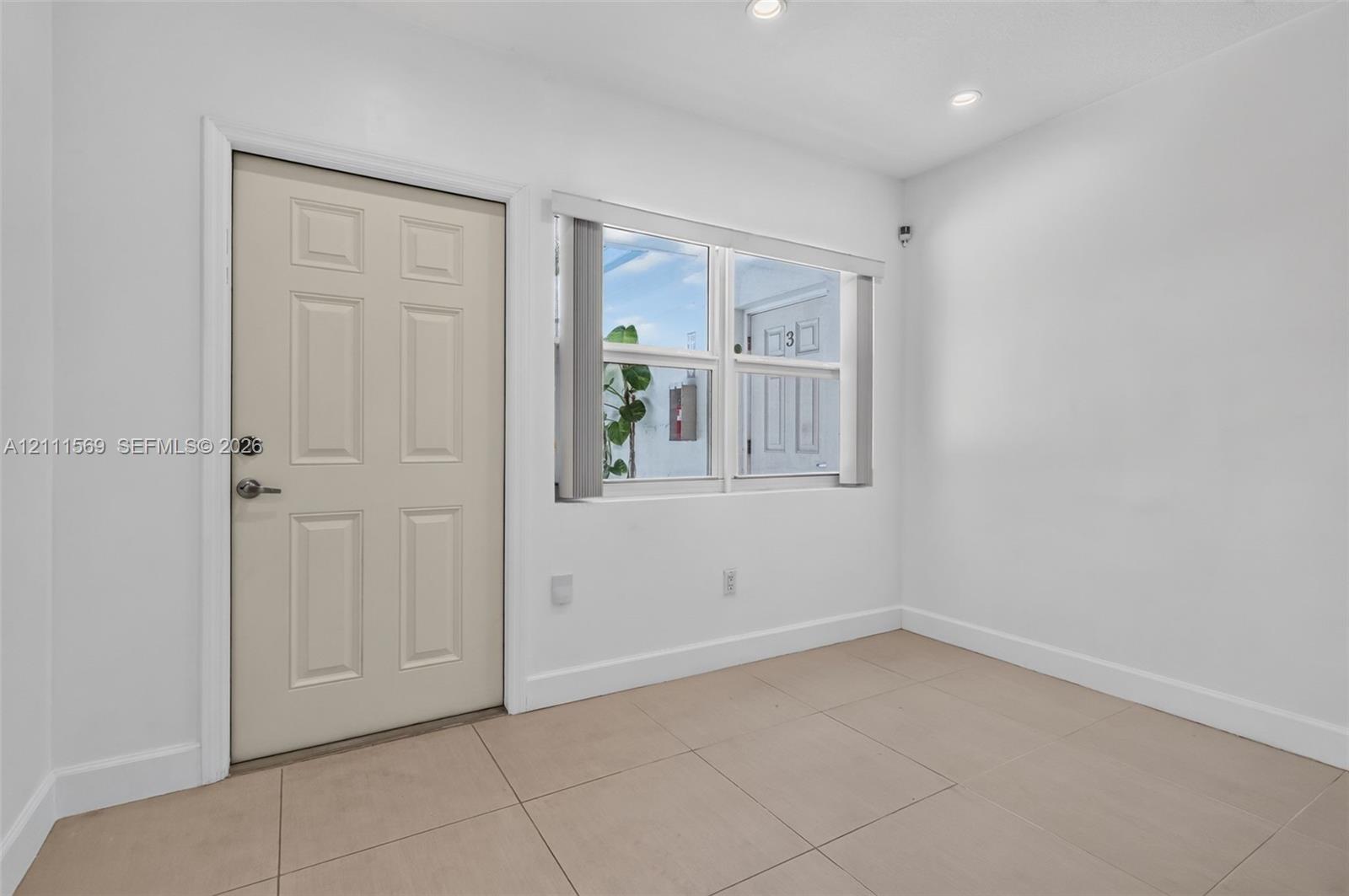 Neutral-toned tile flooring, recessed ceiling lighting, and a multi-panel entry door featuring a brushed metal deadbolt and lever handle