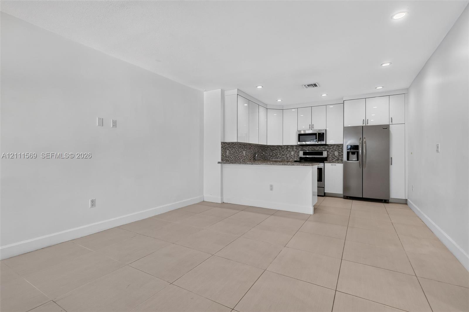 Kitchen featuring white high-gloss cabinetry, stone-finish countertops, mosaic tile backsplash, stainless steel appliances, and large-format tile flooring