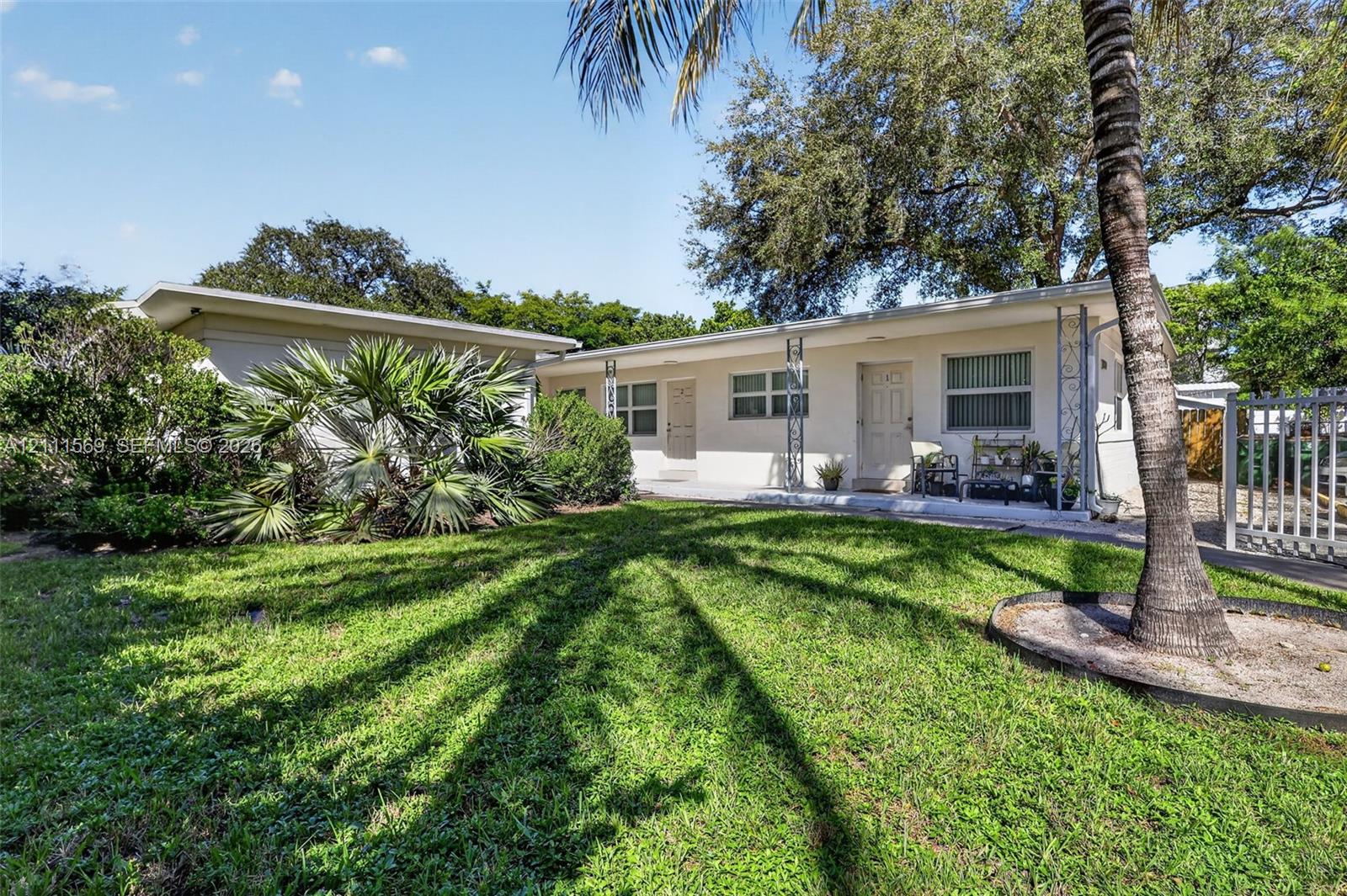 Single-story stucco exterior featuring horizontal sliding windows, metal decorative porch columns, and established palm landscaping