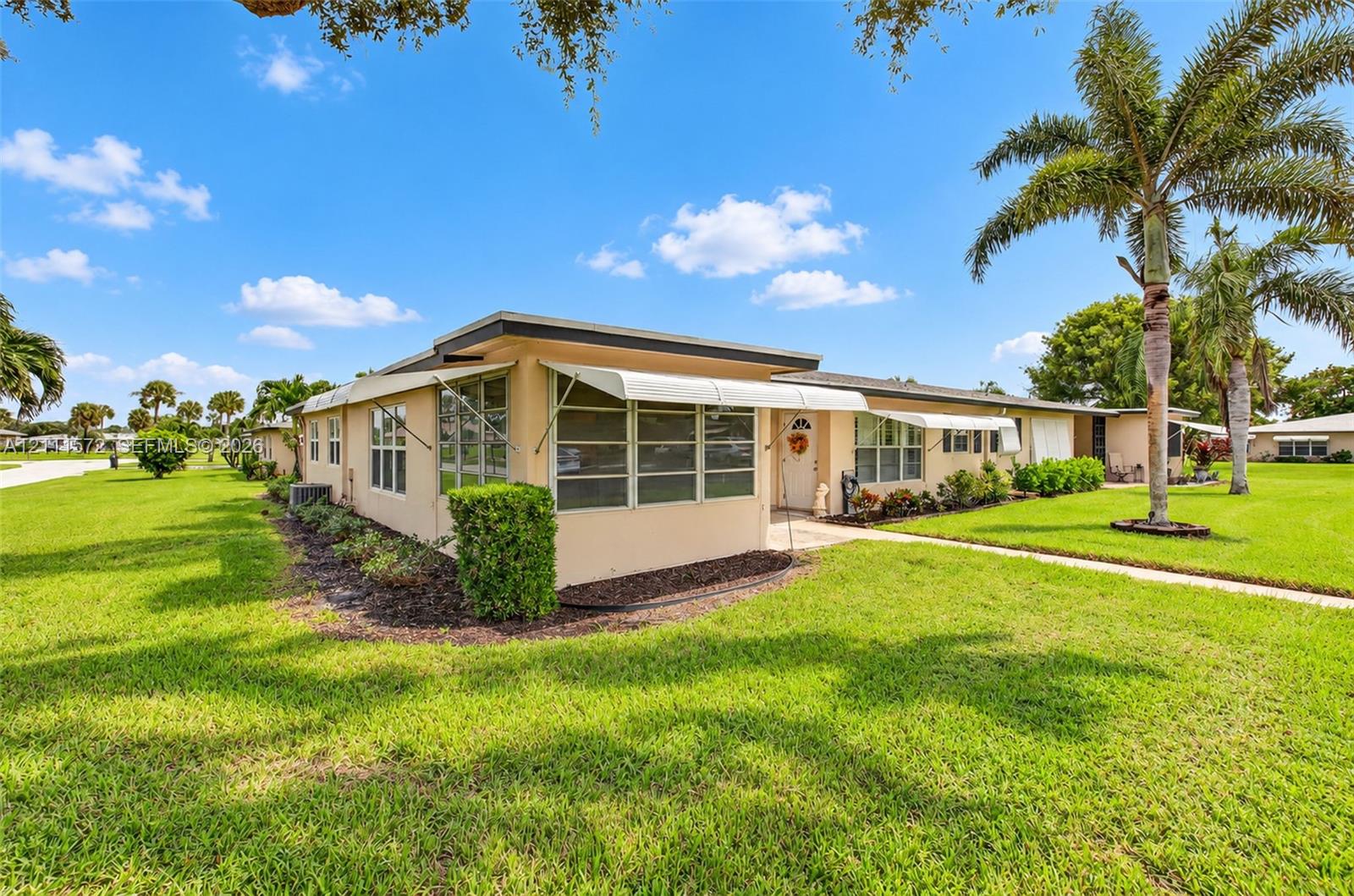 Single-story corner unit villa, multi-pane windows, retractable awnings, and mature palm tree landscaping in a well maintained community