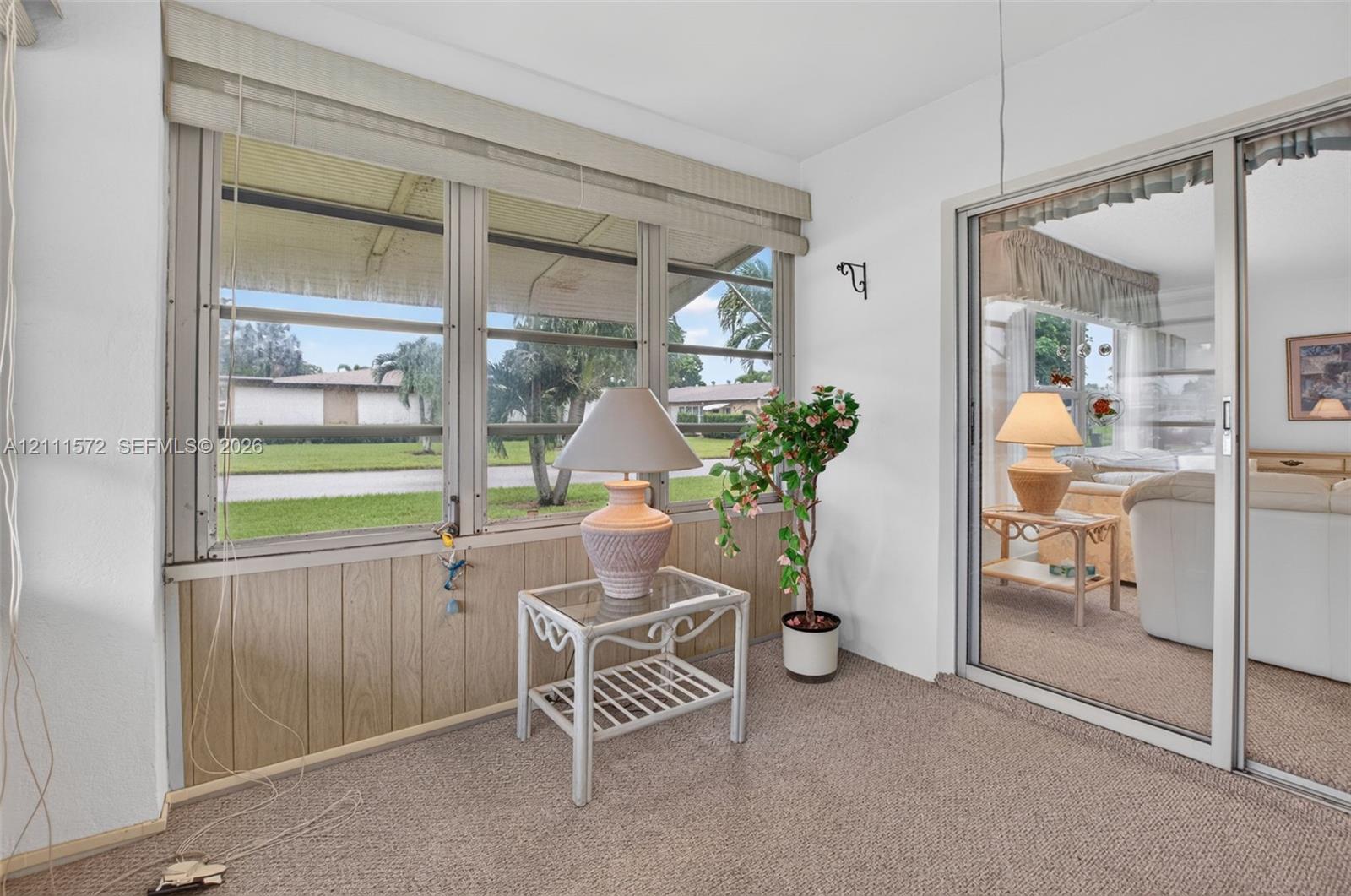 Enclosed sunroom featuring expansive paneled windows, wood-panel wainscoting, berber carpeted flooring
