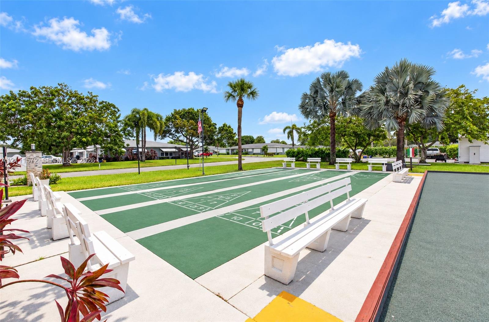 Outdoor shuffleboard court with permanent perimeter bench seating, finished concrete surround, and mature palm trees
