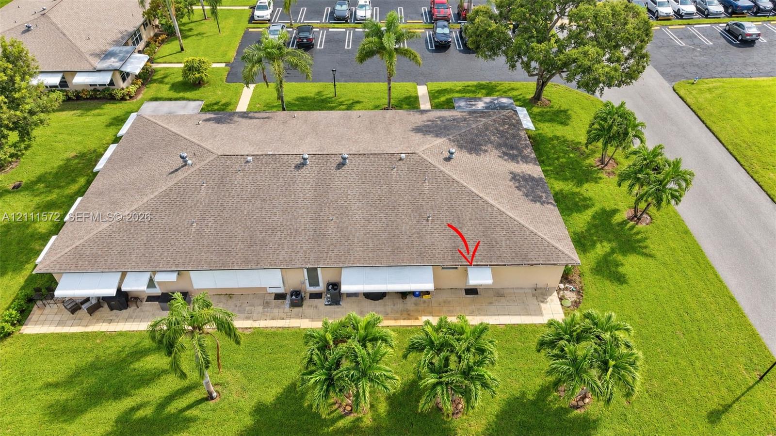 Single-story building featuring a hip roof, exterior stone-tiled patio, and retractable canvas awnings, situated on landscaped grounds with mature palm trees
