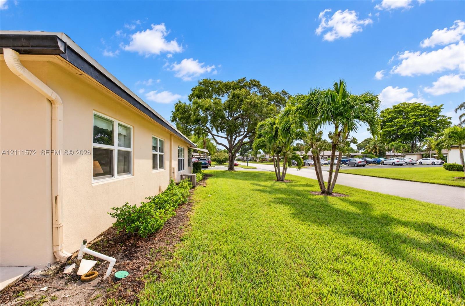 Side of unit featuring dual-pane impact windows, a grass lawn, and mature palm trees