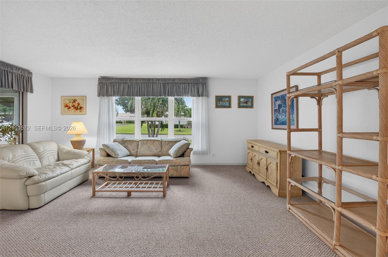 Living area featuring neutral berber carpeting, triple-panel impact window, and recessed sliding glass door leading to enclosed FL room