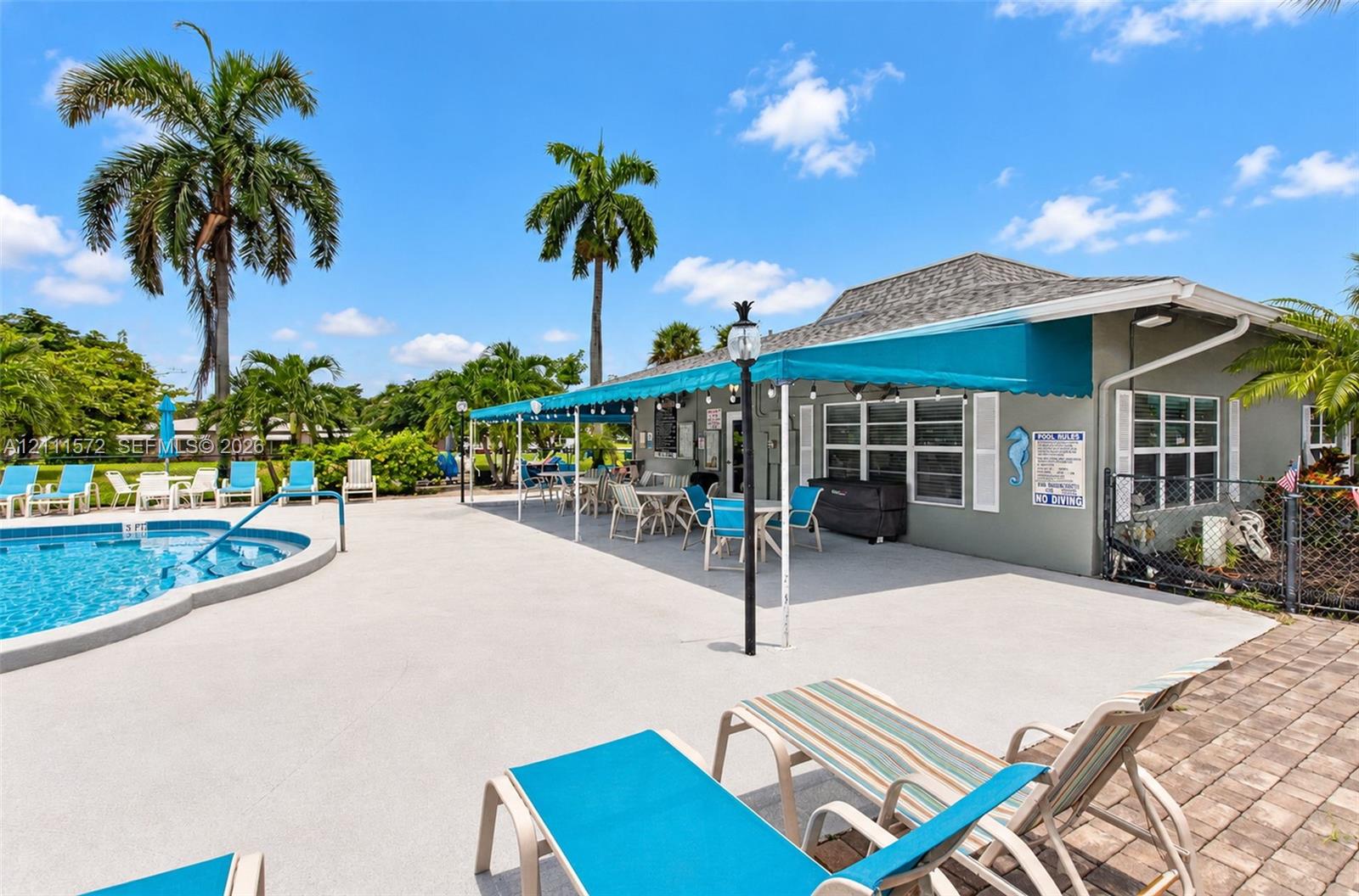 Swimming pool with concrete pool deck, covered patio space, and mature palm trees