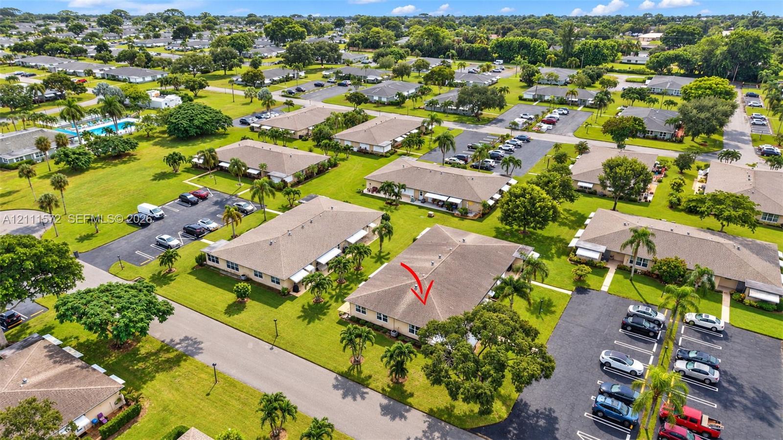 Single-story residential structure featuring a hip roof, exterior wall cladding, and established landscaping with mature palm trees situated within a community of clustered residential units