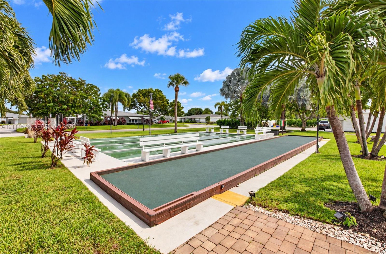 Outdoor recreation area featuring bocce ball and shuffleboard courts, built-in benches, brick paver accents, and mature palm trees