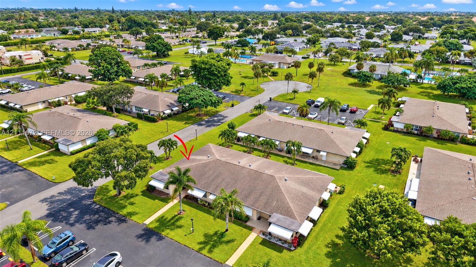 Aerial perspective of a single-story residence featuring a hip roof, exterior awnings, and established tropical landscaping. Amenities are just past the cul de sac.