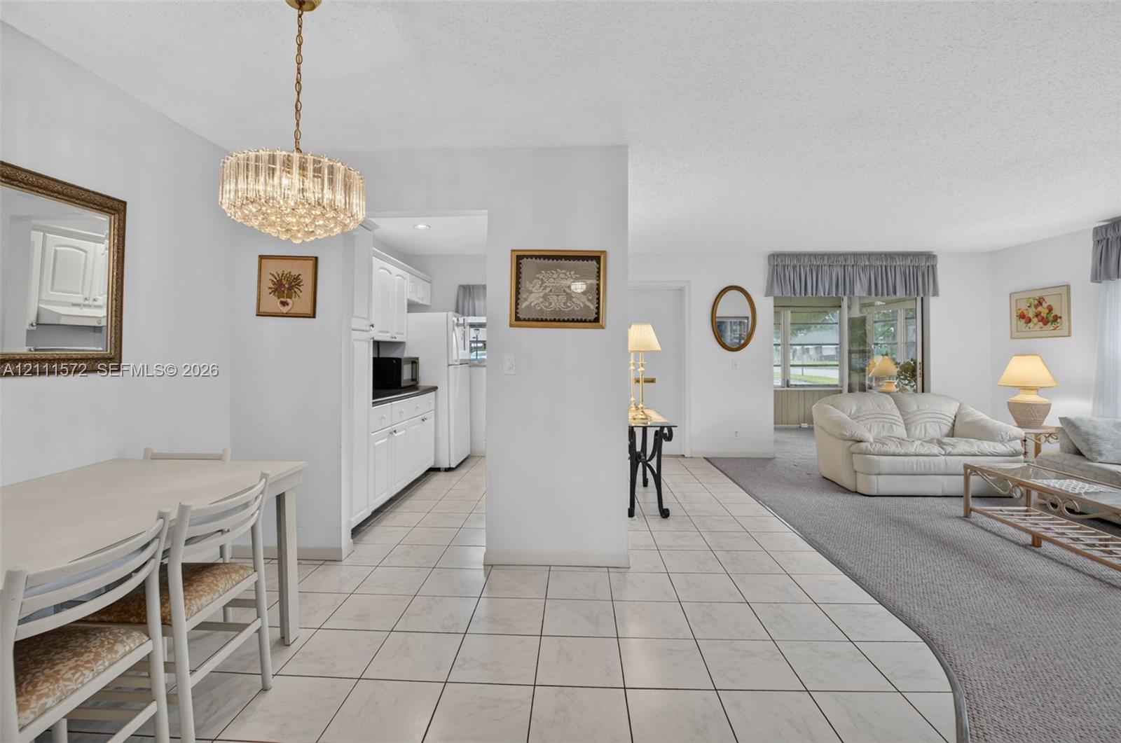 Light and bright spacious interior with neutral tile flooring, crystal pendant light fixture, white cabinetry