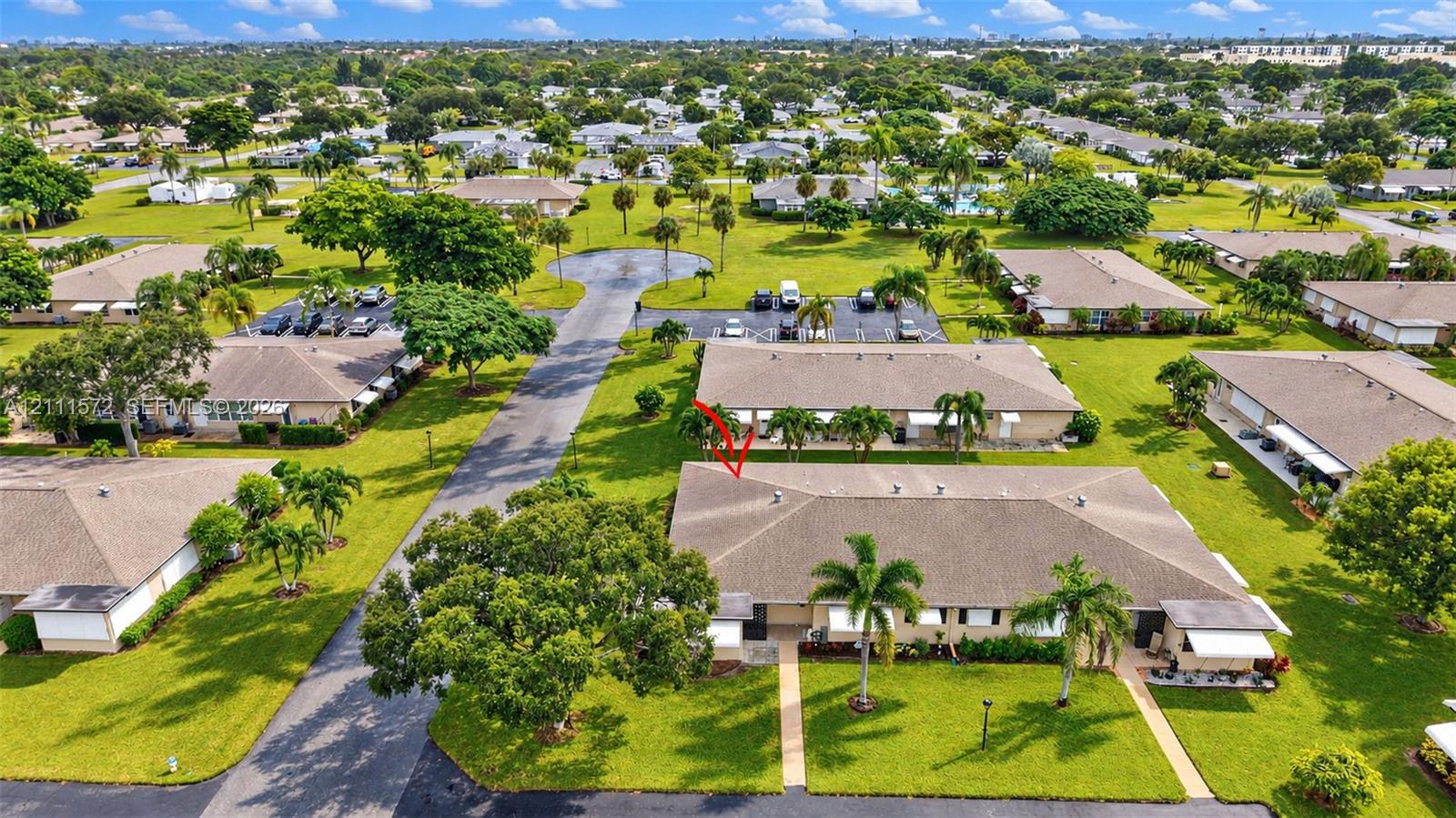 Aerial view of single-story residence featuring a hip roof, exterior shutter accents, concrete walkways, and mature palm trees. Amenities are just past the cul de sac.