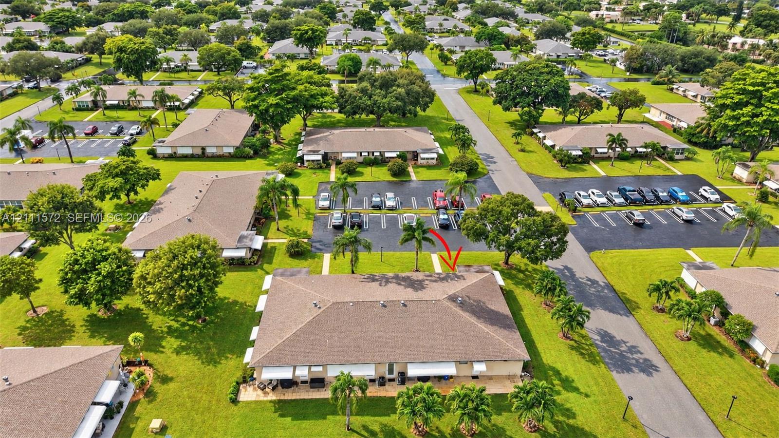 Aerial perspective of a single-story multi-unit structure featuring a shingled roof, paved parking areas, expansive green space, and mature landscaping