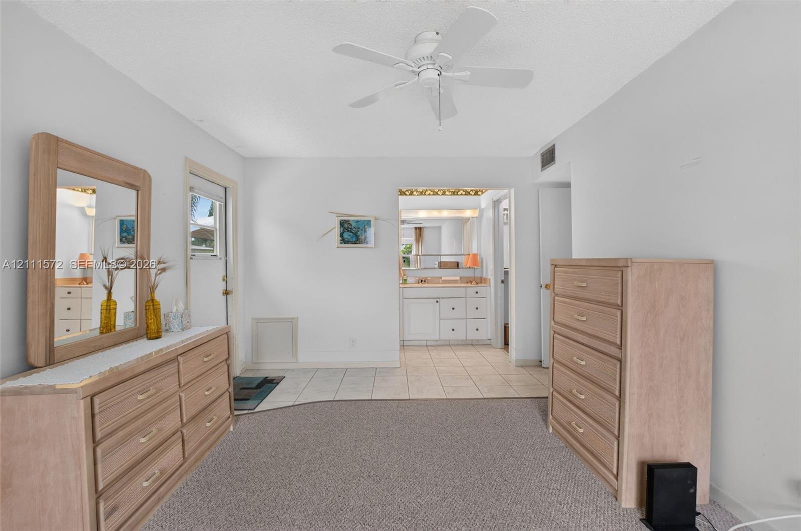 Primary bedroom featuring neutral berber carpeting, ceiling-mounted fan, with tile flooring leading to ensuite bathroom and walk-in closet