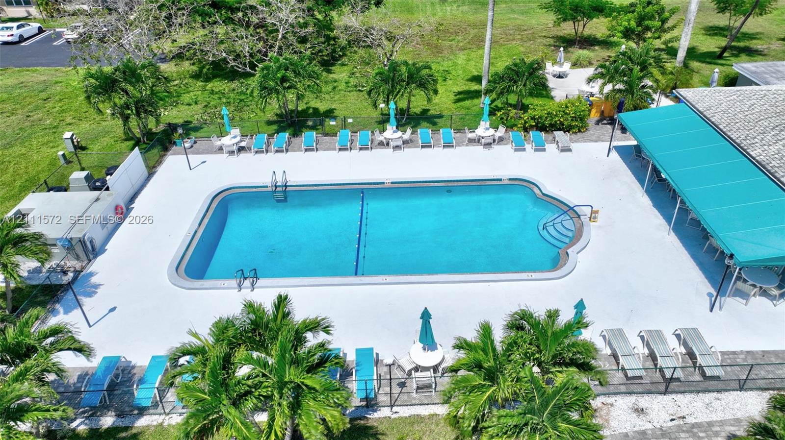 In-ground heated swimming pool with a concrete deck, perimeter fencing, and a covered patio area
