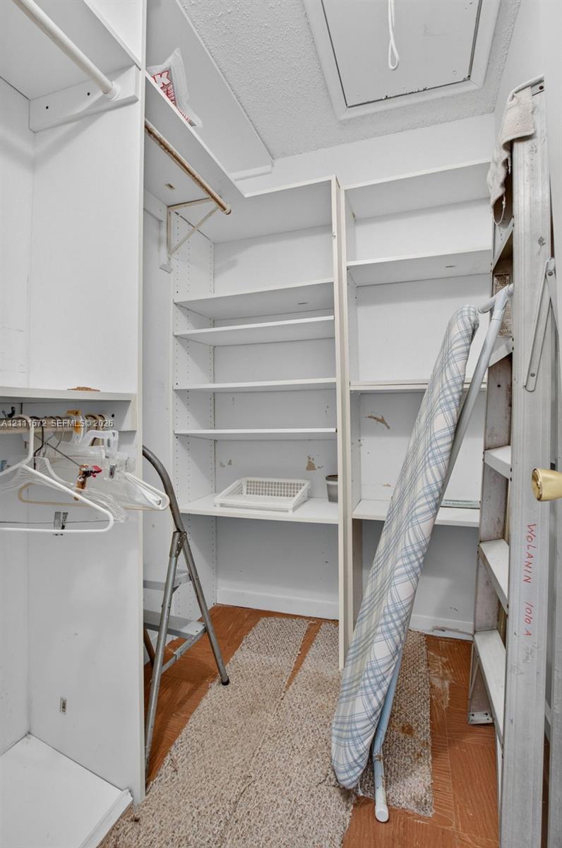 Walk-in closet featuring white built-in shelving, hanging rods, and pull down stairs for attic access and storage
