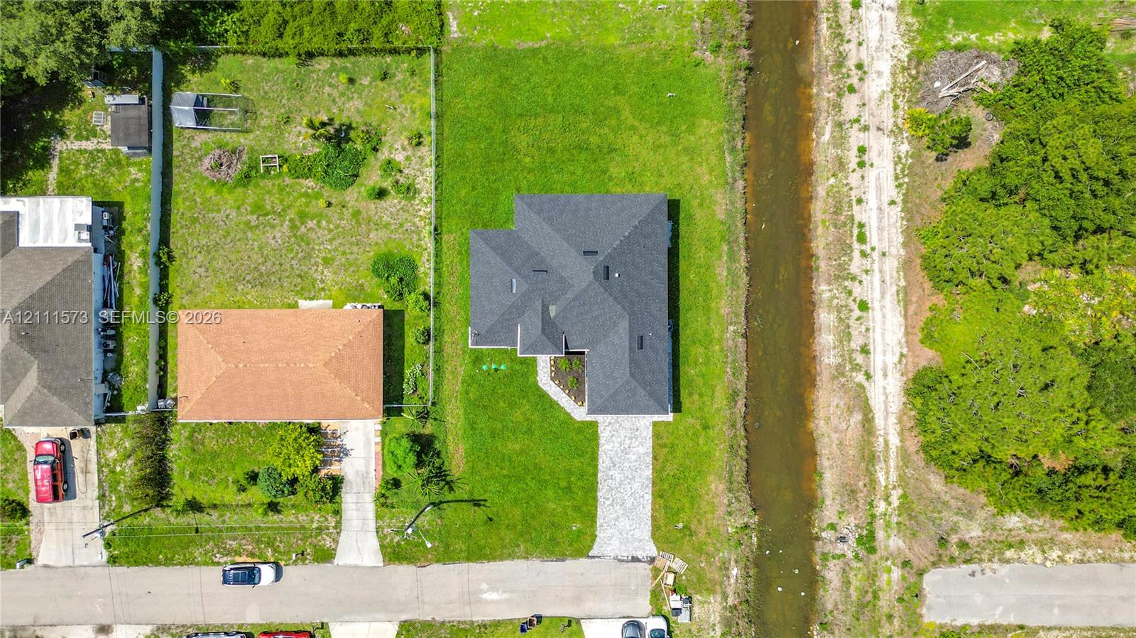 Aerial view featuring a multi-pitched asphalt shingle roof, paved concrete driveway, and expansive grass lot