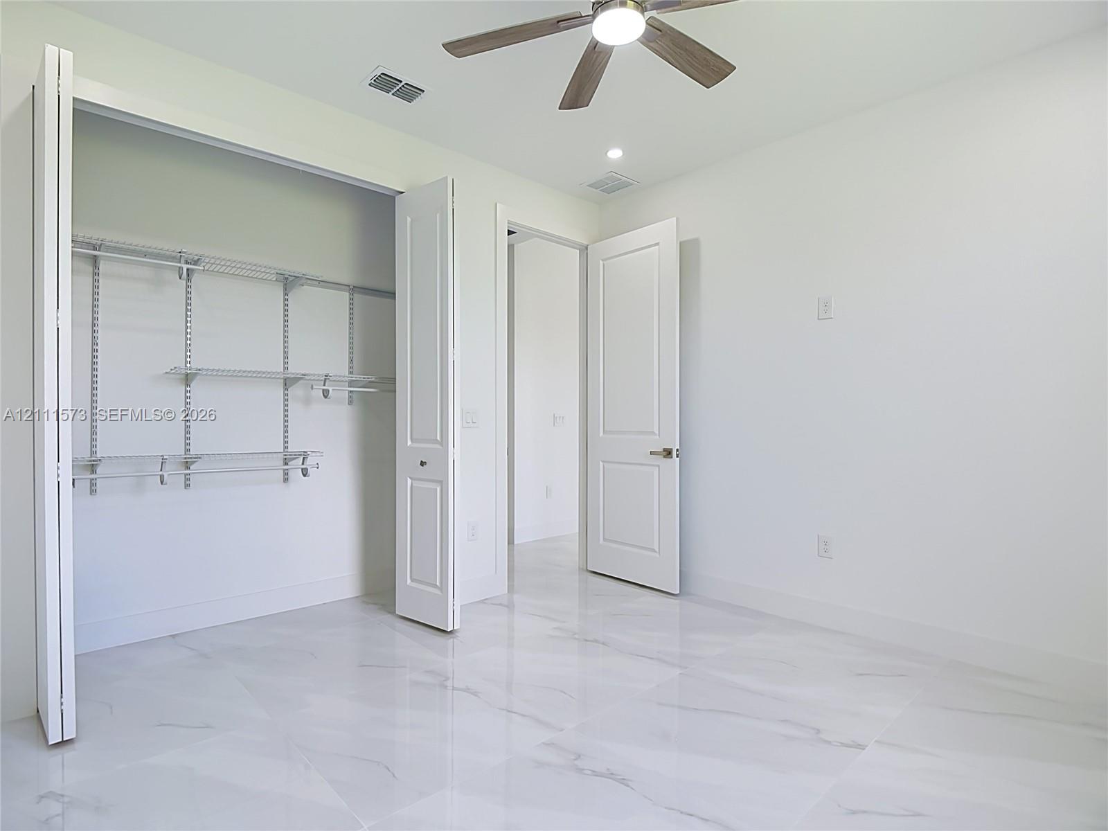 Large-format tile flooring, multi-panel doors, ceiling fan with integrated lighting, and built-in closet shelving