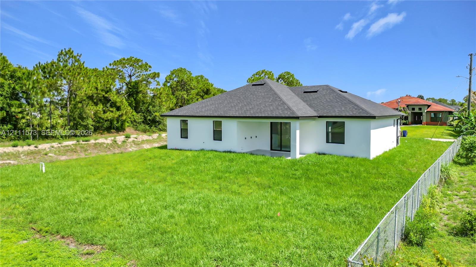 Exterior rear elevation featuring a white stucco facade, a dark shingled roof, a covered concrete patio, and a fenced-in grassy lot