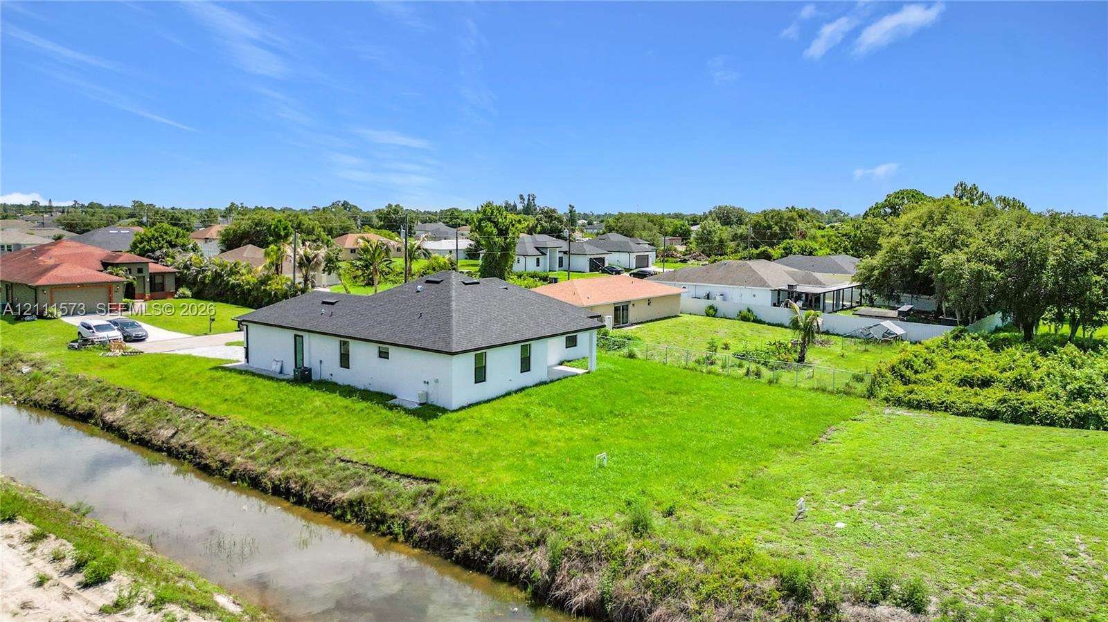 Single-story residence featuring a white exterior, dark shingle roof, expansive lot, and waterfront frontage