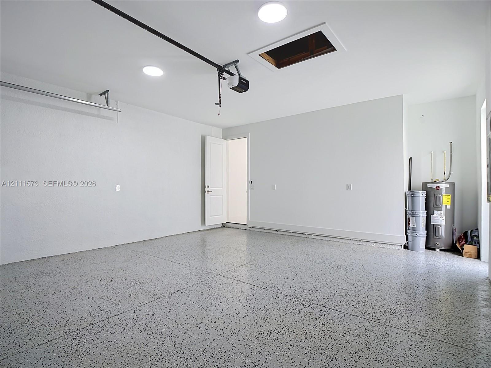 Finished garage space featuring durable epoxy flooring, smooth white walls, recessed ceiling lighting, an automatic garage door opener, and a dedicated water heater