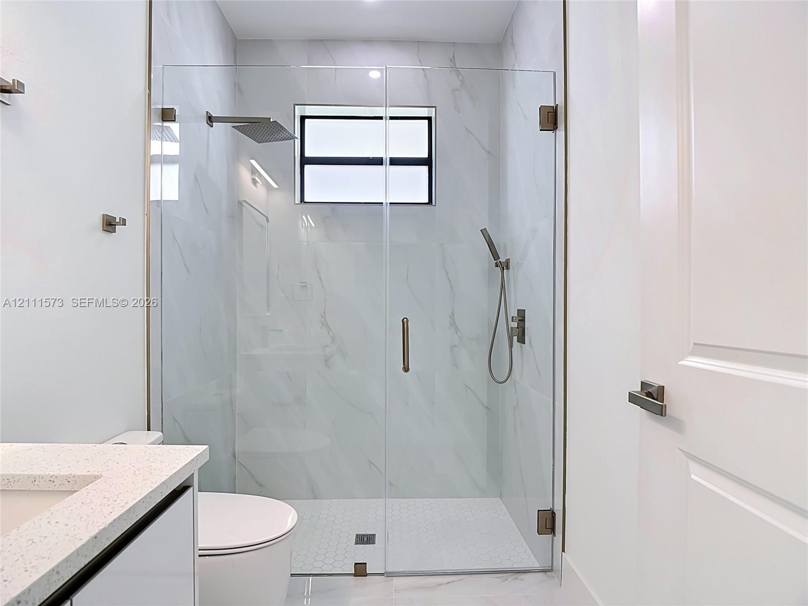 Walk-in shower featuring a frameless glass enclosure, rain-style shower head, handheld sprayer, and large-format wall tile with hexagonal floor tile