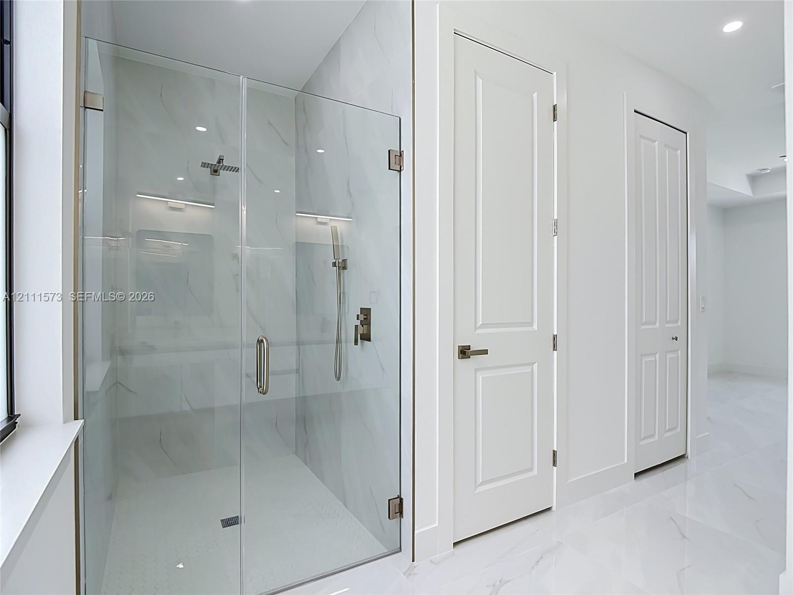 Walk-in shower featuring a frameless glass enclosure, floor-to-ceiling large-format tile surround, rainfall showerhead, handheld sprayer, and polished metallic fixtures