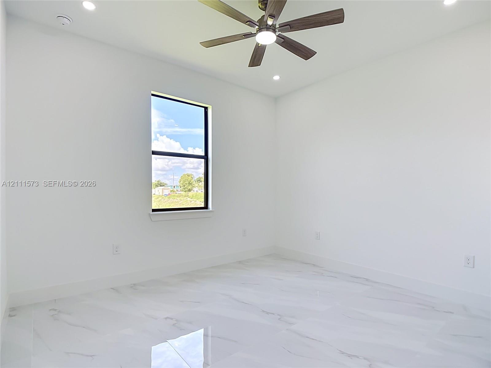 Neutral-toned interior space featuring white-finish tile flooring, recessed lighting, a ceiling fan with integrated lighting, and a single-pane window with a black frame