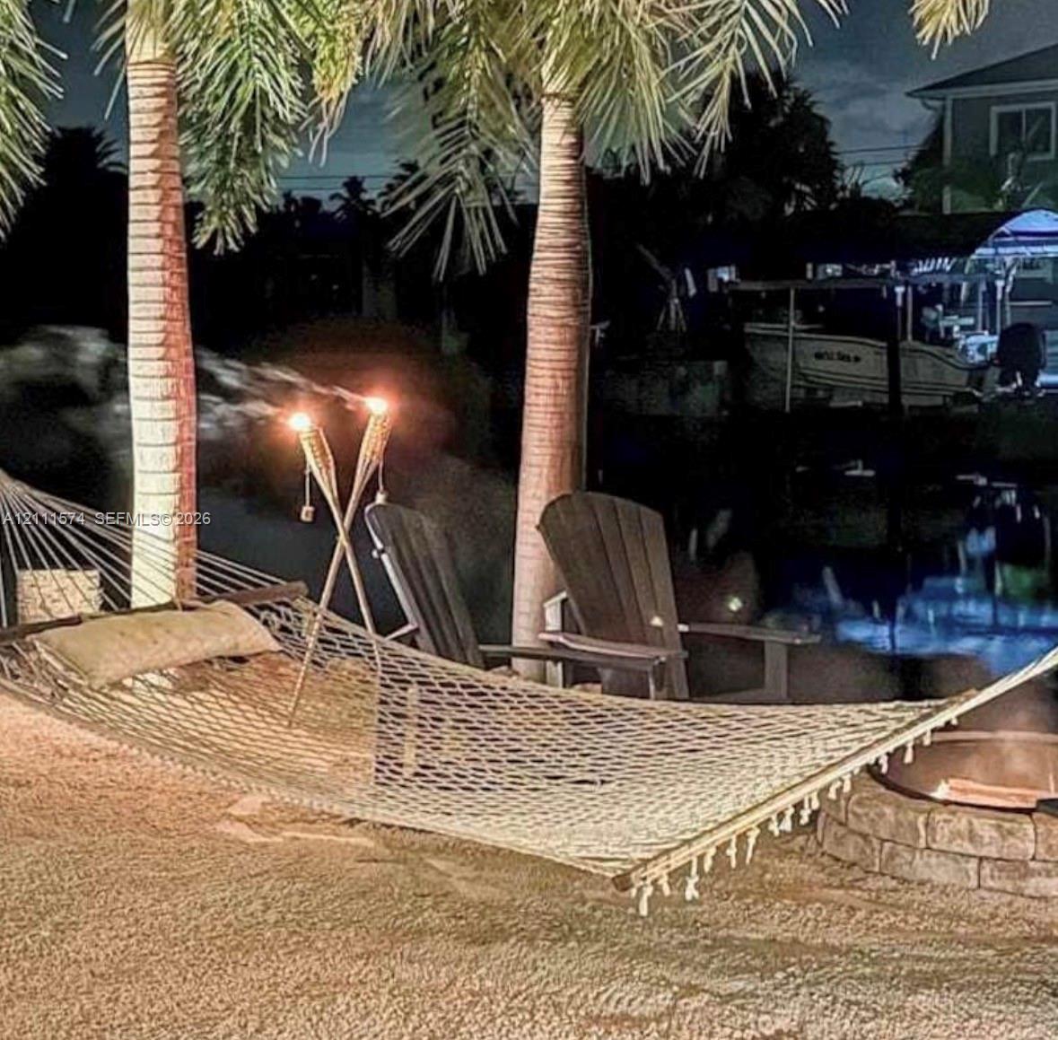 Waterfront backyard featuring mature palm trees and a circular stone fire pit