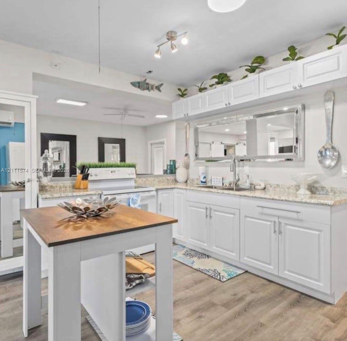 Kitchen featuring white shaker-style cabinetry, stone-finish countertops, wood-finish flooring, a stainless steel undermount sink, and a center island with a wood-tone surface