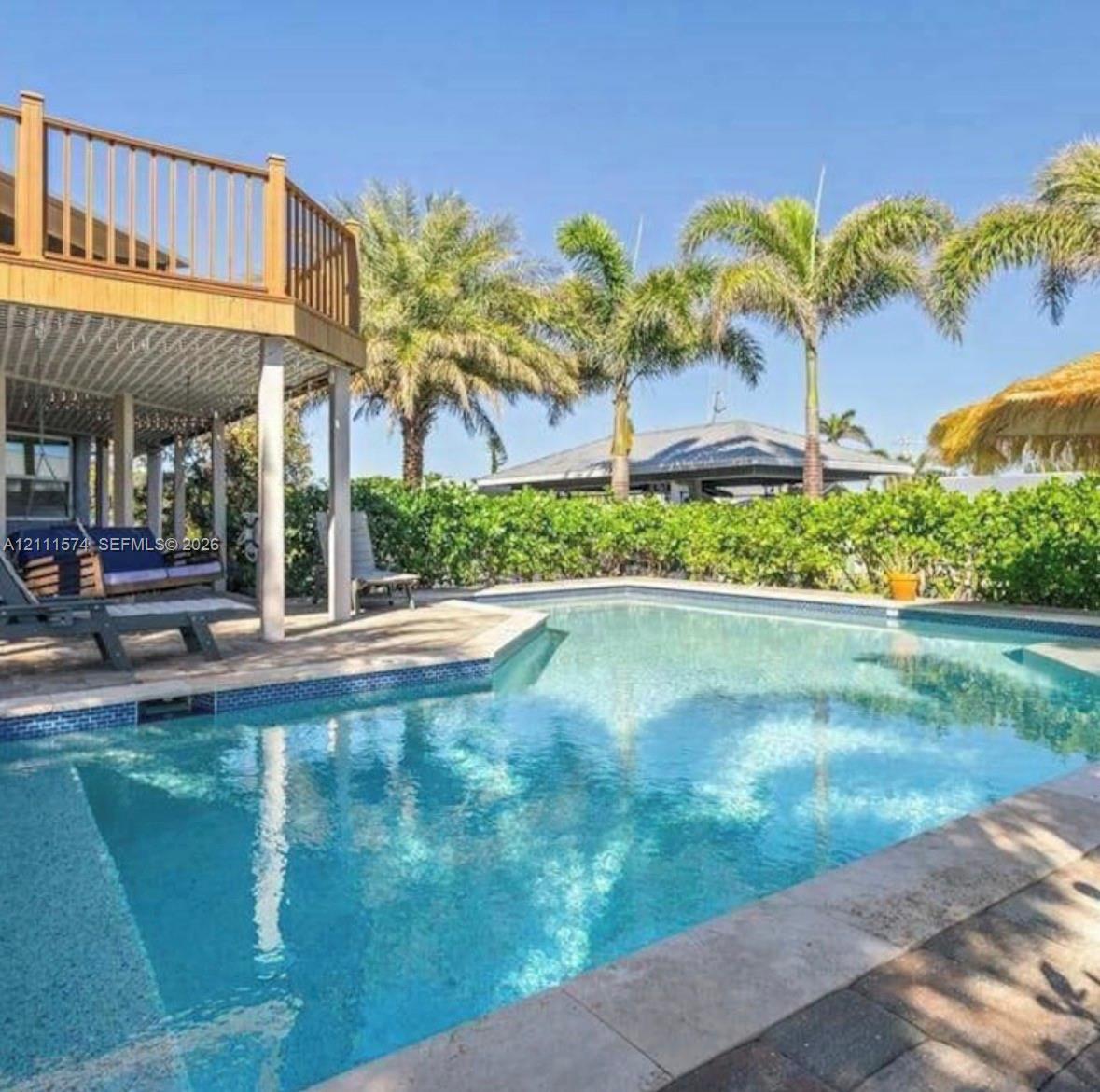 In-ground swimming pool with tile border, elevated wood-finish deck, stone paver pool deck, and mature palm trees