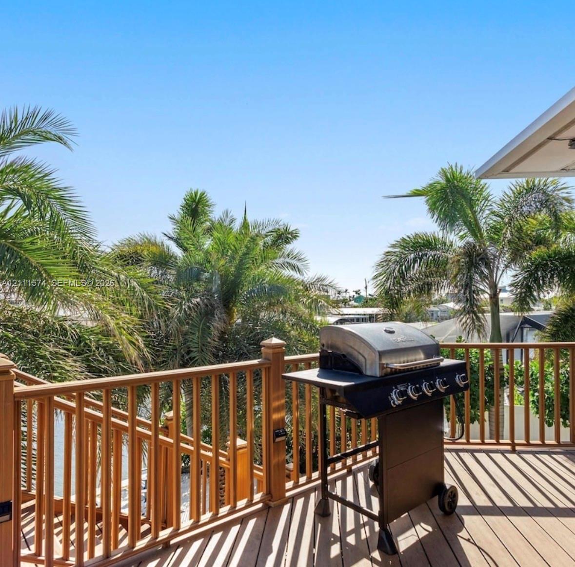 Elevated deck featuring synthetic composite decking, vertical wood-finish railing, and mature palm trees