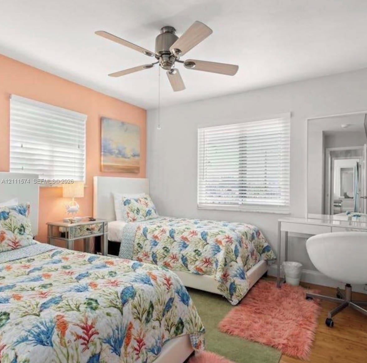 Bedroom featuring a brushed nickel ceiling fan, wood-finish flooring, two large windows with installed blinds, and a built-in full-length mirror