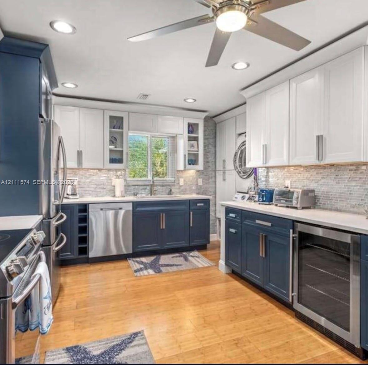 Kitchen featuring two-tone custom cabinetry, stone mosaic backsplash, quartz countertops, stainless steel appliances, and wood-finish flooring