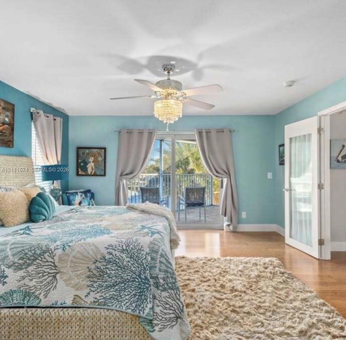 Crystal-style chandelier with a central ceiling fan, wood-finish flooring, and glass-paneled entry door