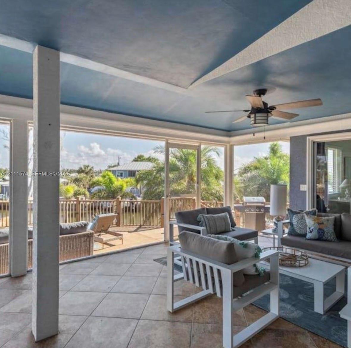 Screened-in porch featuring large-format tile flooring, blue painted ceiling, integrated ceiling fan, and extensive screened walls